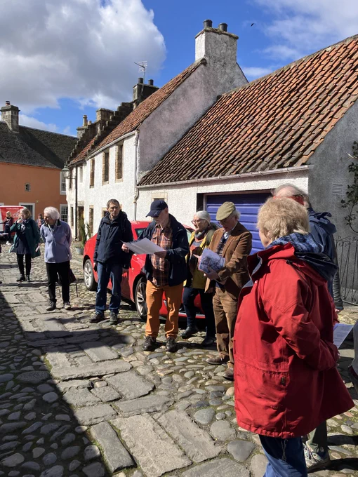 People in front of harled and pantiled houses on a stone street surface.
