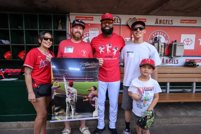 Kayleigh K. and her family smile for a photo with Jo Adell in the Angels dugout as one of her family members holds up an autographed poster of the Jo Adell Third Home Run Robbery, as captured by Kayleigh in the stands. 