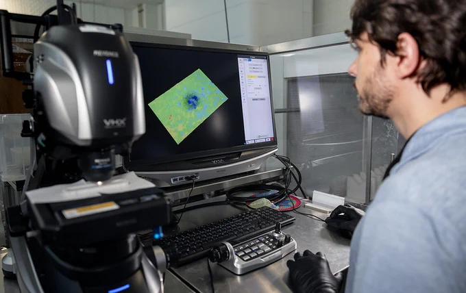 A person in a laboratory setting is observing a screen displaying a 3D visualization of data. 