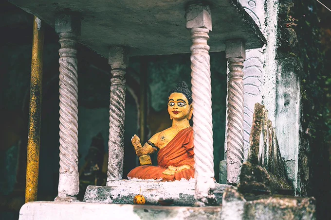 A brightly painted but badly cracked statue of a seated Buddha in a small four-pillared shrine.