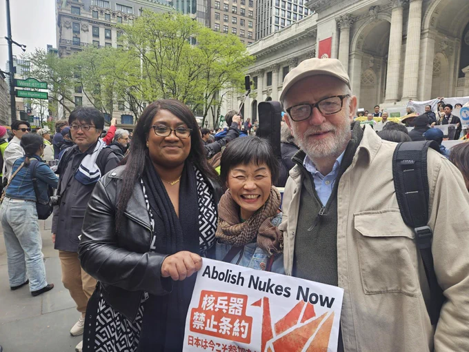 Bell Riberio-Addy and Jeremy Corbyn stand with a woman at a protest. They are holding a poster with an origami crane and "Abolish Nukes Now" on it.