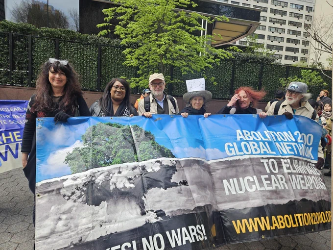 Bell Ribeiro-Addy and Jeremy Corbyn stand with people behind a banner for the Abolition 2000 Global Network