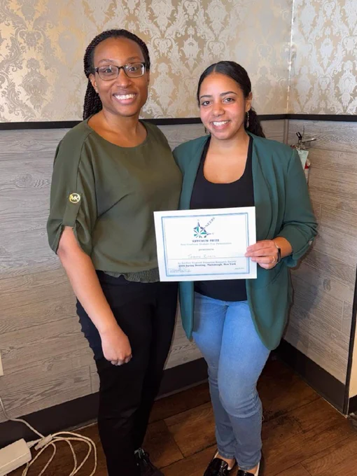 Two people standing indoors, one holding a certificate of achievement