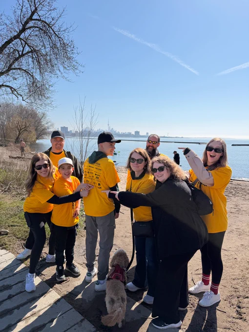 PSHSA team members and their loved ones, pointing at the PSHSA logo on the back of the Steps for Life shirts. 
