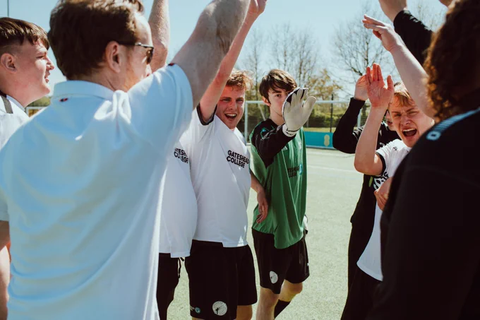 A team standing in a circle in high spirits, lifting their hands together.