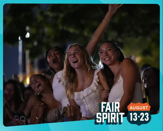 Four women singing along to a song at the Susan Knapp Amphitheater. Around the edge of the graphic is a blue border with "Fair Spirit August 13-23" in the bottom right corner. 