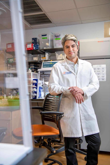 A scientist wearing a lab coat stands in a laboratory, surrounded by shelves of scientific equipment and supplies.