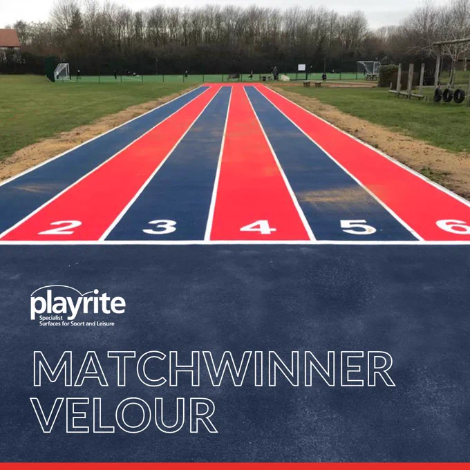 A vibrant outdoor running track with alternating red and blue lanes numbered 2 to 6, surrounded by green grass and trees.