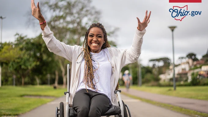 A woman in a wheelchair holds her hands up in a gesture of celebration.