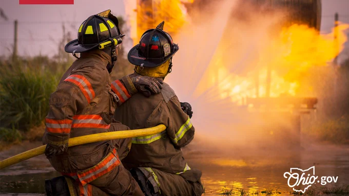 Two firefighters hold a hose together while they battle a nearby blaze.