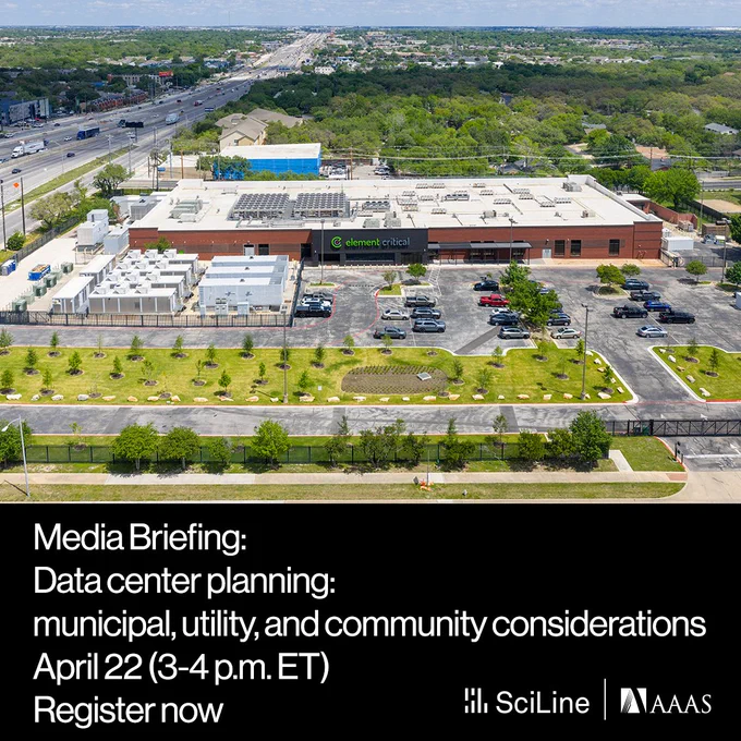 A data center building with a parking lot is located just off a highway with green trees behind it.