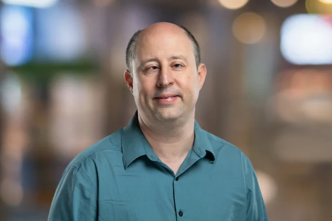 Jonathan Avila's headshot. Jonathan wears a teal green professional collared shirt and smiles slightly at the camera. 