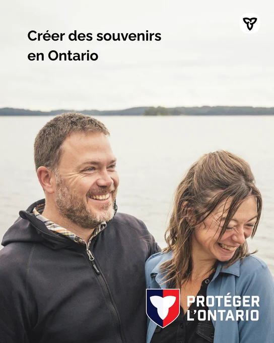 Deux personnes se tiennent côte à côte au bord d’un lac, avec une eau calme et une rive lointaine visibles derrière elles sous un ciel couvert. L’une porte une veste sombre et l’autre une chemise bleu clair. Le texte sur l’image indique « Créer des souvenirs en Ontario », avec le logo du bouclier « Protéger l’Ontario » affiché dans le coin inférieur.