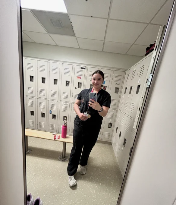A person in a medical uniform standing in a locker room. A pink water bottle sits on a bench behind the person.