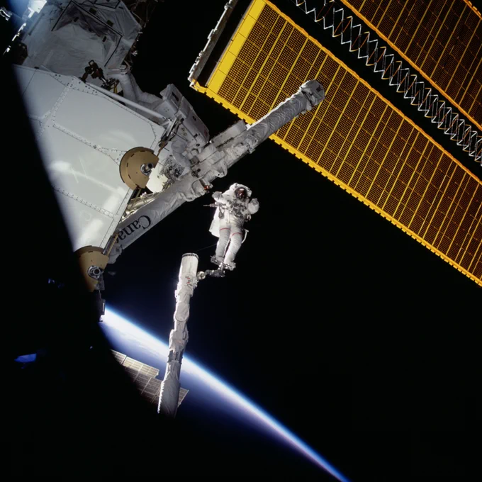 Through the window of space shuttle Endeavour, Chris Hadfield is seen in the center of the frame with his feet in the portable foot restraint (PFR) at the end of the orbiter's remote manipulator system (RMS). Above him, we see one of the International Space Station's solar arrays, and in the lower left corner, the limb of Earth. Astronaut Scott Parazynski, mission specialist, is seen at left near the Spacelab pallet. Photo ID: sts100-714-027. Credit: NASA