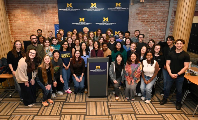 A group of people smiling and standing together in a room with a podium. The backdrop displays the SEAS logo. 