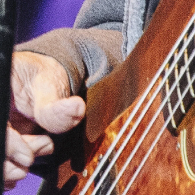 A close up photo of someone playing the bass guitar. The bass is wooden and orange with a hand looking like it's about the pluck one of the strings.