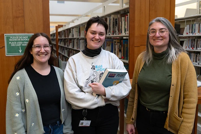 three library workers standing together in a library and smiling at the camera