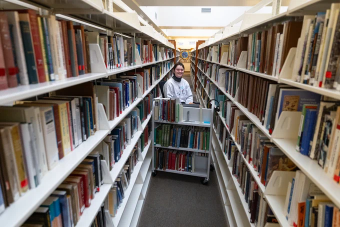 A person in the middle of a long book aisle in a library