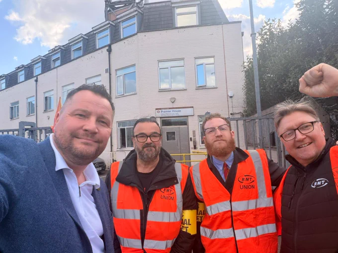 Four people wearing RMT Union high-visibility vests stand outside a building with a sign reading 'Pioneer House'.