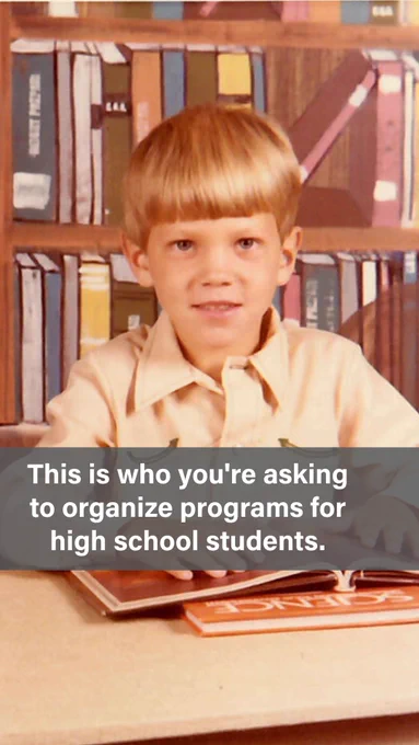 A vintage school portrait of a young boy with a straight blond bowl cut, wearing a light tan collared shirt, seated in front of a painted bookshelf backdrop with a science textbook visible on the desk in front of him. Text overlay reads: "This is who you're asking to organize programs for high school students."
