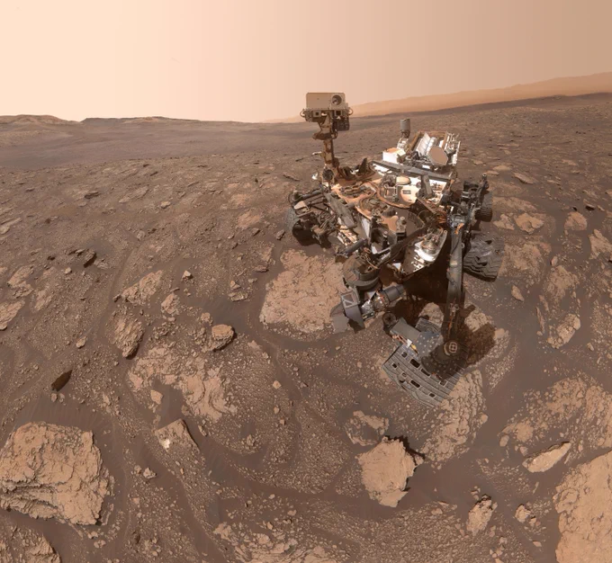 A selfie of the Curiosity rover on the surface of Mars. The rover is parked on a plain of mostly flat, layered rocks.
