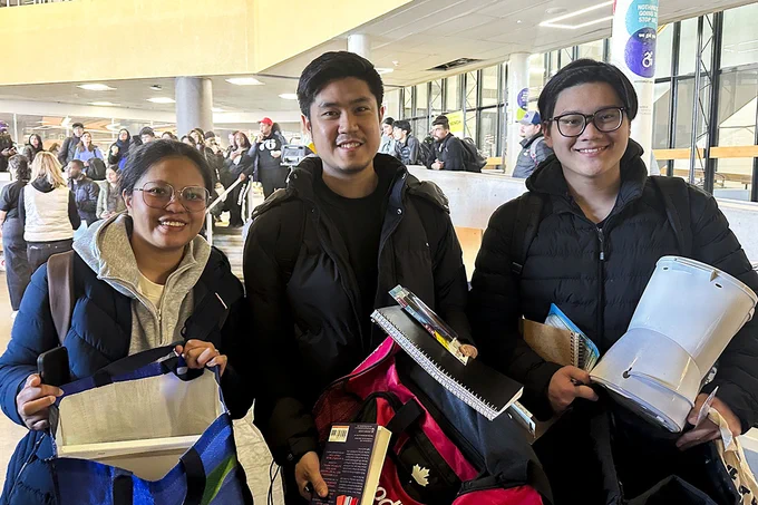 Three similing people are holding various items.