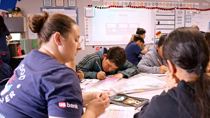 U.S. Bank volunteer working with kids at a table in a classroom.