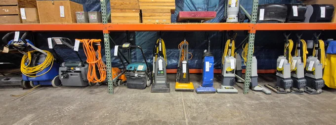 Various pieces of custodial equipment lined up under racking at Surplus.