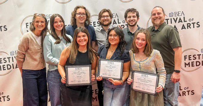 A group of smiling individuals poses in front of a "BEA Festival of Media Arts" banner. Three people in the front hold certificates.