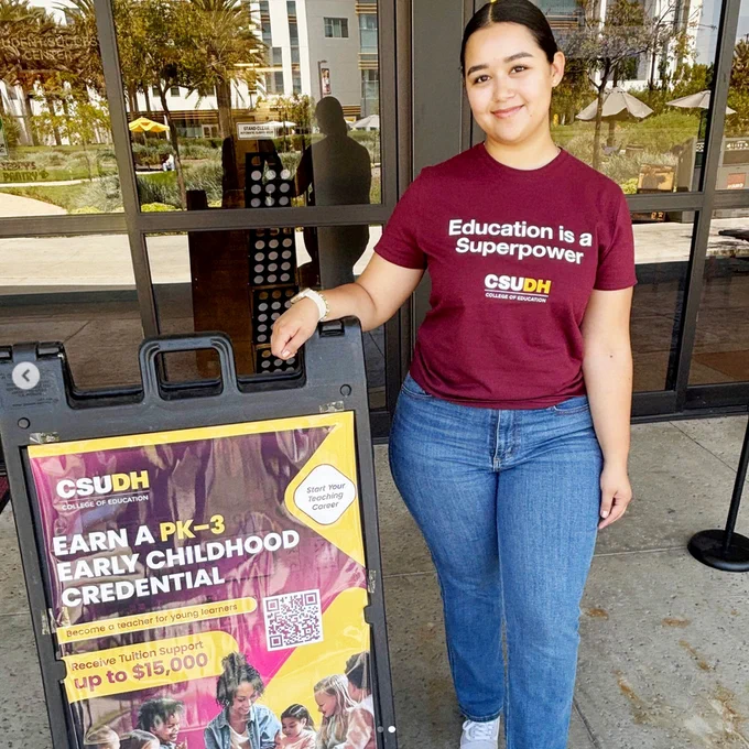 Sabrina standing next to a sandwich board that has a poster about the PK-3 credential program
