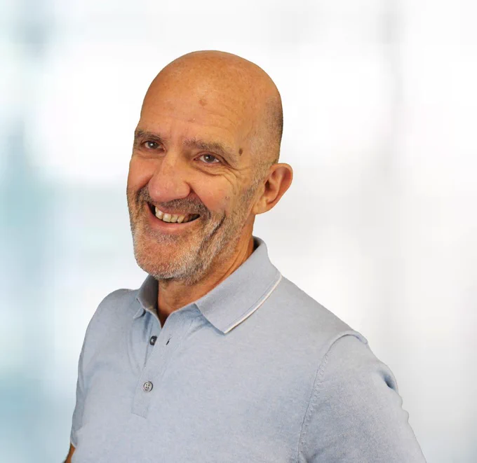 Noel Duffy smiling towards the camera in a blue polo shirt.