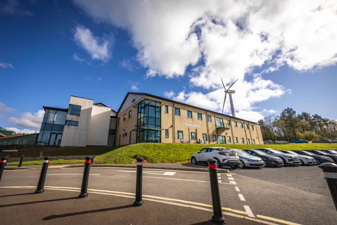 Trust Headquarters building with a wind turbine, cars, and a blue sky with clouds.