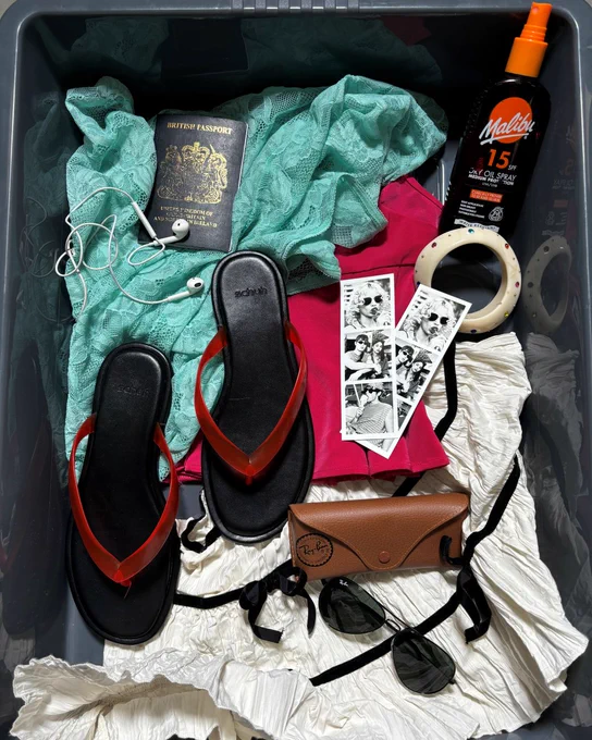 An image of a pair of black and red schuh Truffle Toe Post sandals sitting in a black tray surrounded by a passport, sun screen and accessories.