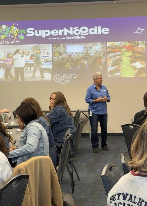 Woman standing in the front of the room in front of a slide deck titled "Super Noodle"