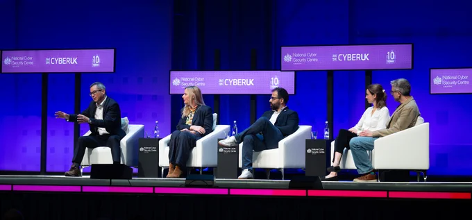 5 panellists sit in chairs next to each other at the Ecosystem Plenary on the stage at Cyber UK. 