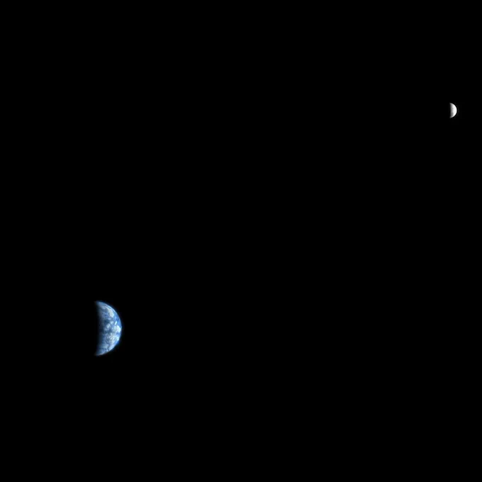 A crescent Earth and Moon seen from a great distance against the emptiness of space. Blue water and white clouds make the Earth immediately recognizable as home.