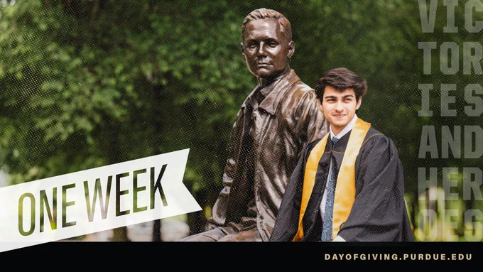 A person in graduation attire sits beside the bronze statue of John Purdue.