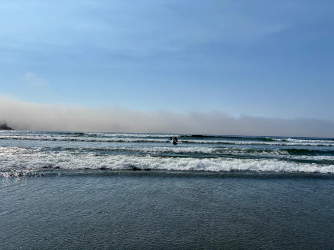 Waves rolling onto a beach under a blue sky with haze on the horizon.