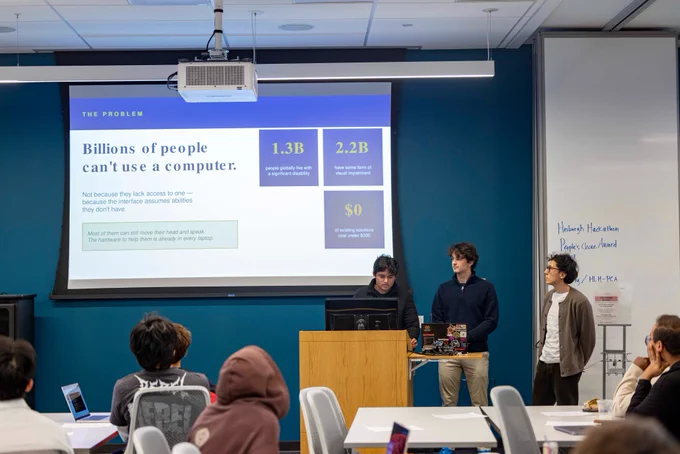 Students present at the 2026 Hesburgh Libraries Hackathon in a Library meeting room. A screen in the background shows images from their project.