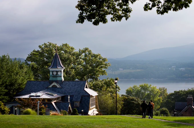 Summertime scene at Mount Saint Mary College with Whittaker Hall to the left and a group of students walking down a path. The Hudson River and mountains are seen in the distance. 