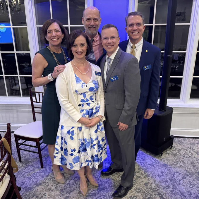 
Five people pose together smiling in an elegant event space with blue uplighting. They are dressed in formal attire and several wear Zero Abuse Project name badges. Two women stand on the left, and three men stand to the right and center.