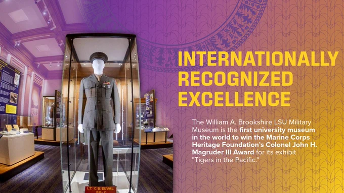 The image shows a military uniform displayed in a glass case at the William A. Brookshire LSU Military Museum. Surrounding informational panels highlight its recognition for winning the Marine Corps Heritage Foundation’s Colonel John H. Magruder III Award. The background features ornate purple and yellow museum decor, with large text stating "Internationally Recognized Excellence.