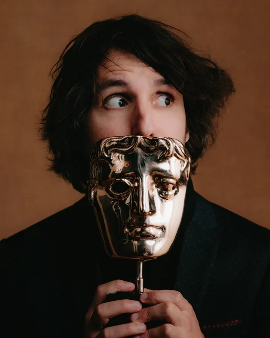Guillame Broche poses peeking over his BAFTA. He is looking sideways cheekily.