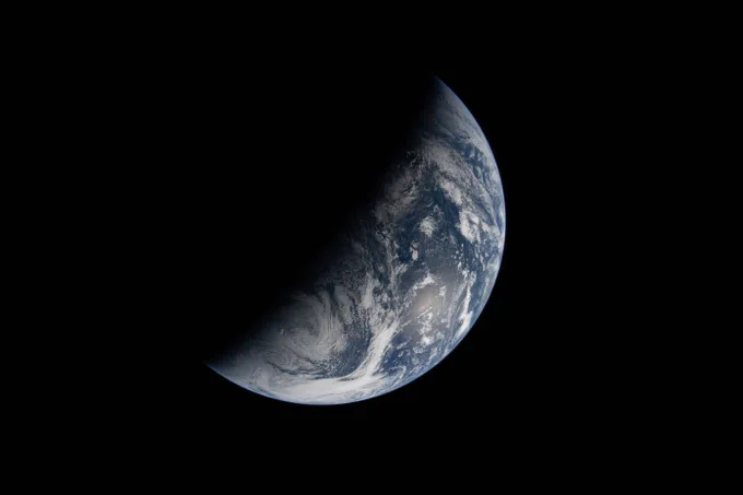 Image of Earth bisected by the terminator line. The terminator divides Earth\u2019s surface diagonally, shrouding the top left half in darkness. Earth\u2019s illuminated surface is mostly blue and covered in swirling white clouds. Credit: NASA