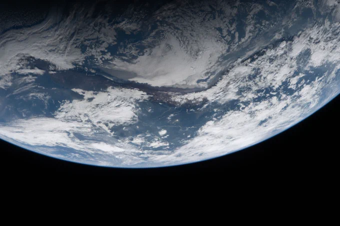 Image of Earth from the Artemis II mission. Earth fills the top half of the image. Through the gaps in white cloud cover, green and brown land masses are visible, as is blue water. Credit: NASA