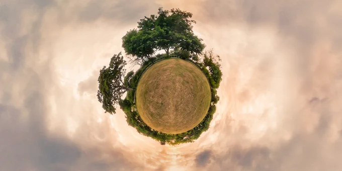 Tinyplanet panorama of a circular helipad surrounded by trees, wrapped in a soft sunrise sky with warm orange light and scattered pastel clouds, giving a calm, early-morning atmosphere.