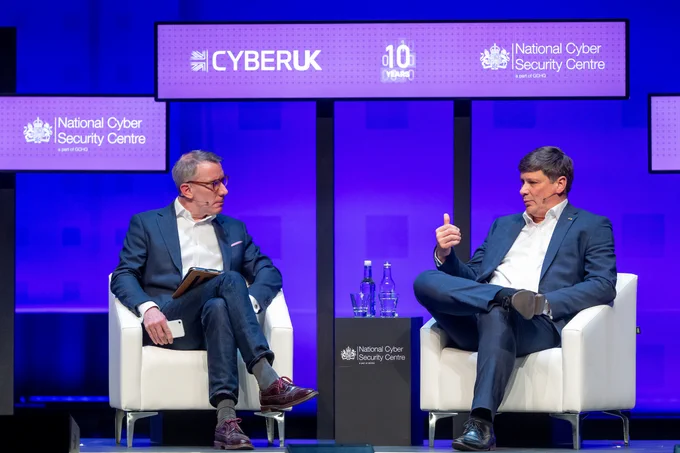 Paul Chichester and Geoff White sit on chairs next to each other on the Cyber UK stage. 