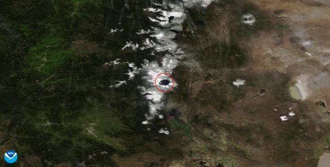 Satellite image of a lake (within a red circle) amid snow-covered mountains with the NOAA logo in the bottom left-hand corner.