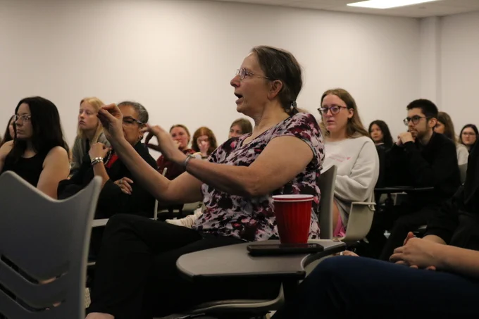 Cynthia Cress asking a detailed question to Dr. Davis E. Henderson. In the background are students and faculty.